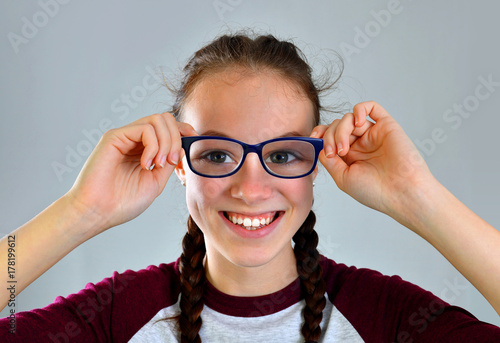 Cheerful pretty young woman with glasses on gray background.