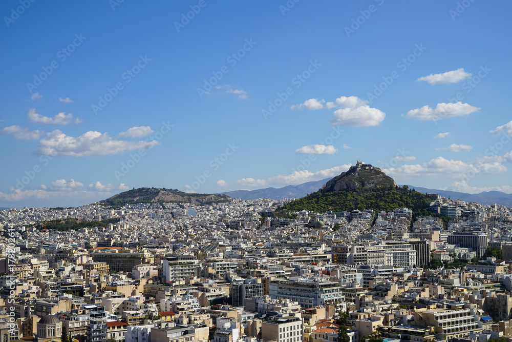 View of Athens city from Acropolis showing white buildings architecture, Mount Lycabettus, blue sky and floating white cloud background