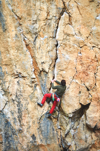 male rock climber climbs on a rocky wall at winter sunny day. Man climber in warm clothes on yellow cliff.