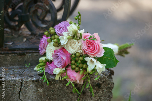 Roses and berries bridal bouquet positioned on a rustic, old iron fence under overcast light with blurred background
