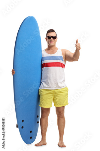 Young man holding a surfboard and making a thumb up gesture