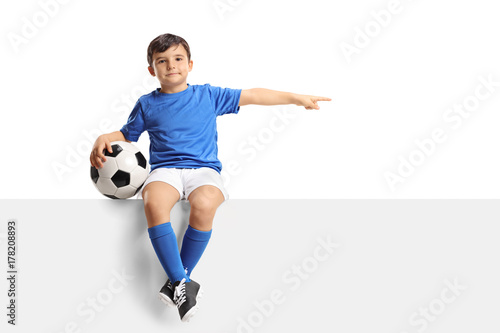 Fototapeta Naklejka Na Ścianę i Meble -  Little footballer sitting on a panel and pointing