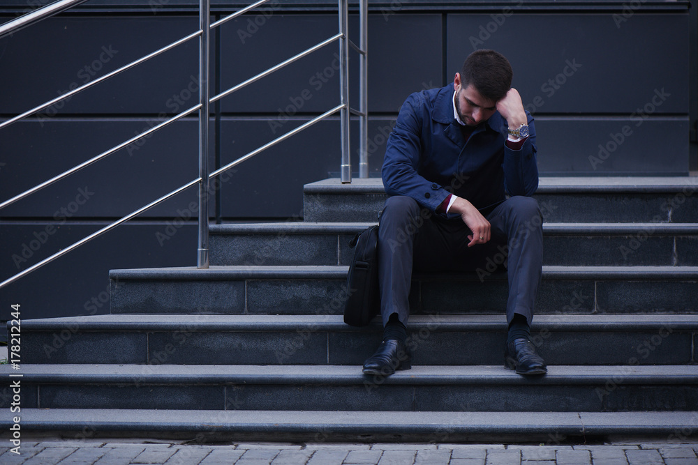 The concept of the bankruptcy of a business man sitting on stairs on the street holding his head The concept of the bankruptcy of a business man sitting on stairs on the street holding his head