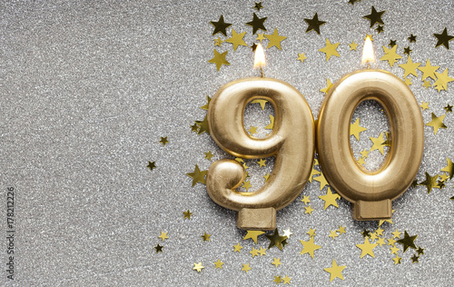 Number 90 gold celebration candle on star and glitter background