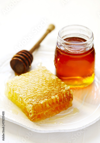 Honeycombs with honey, honey in glass jar and wooden honey dipper on plate
