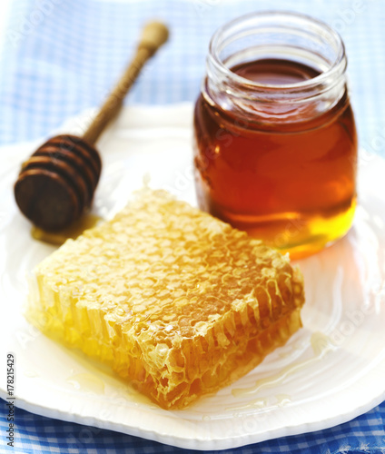 Honeycombs with honey, honey in glass jar and wooden honey dipper on plate