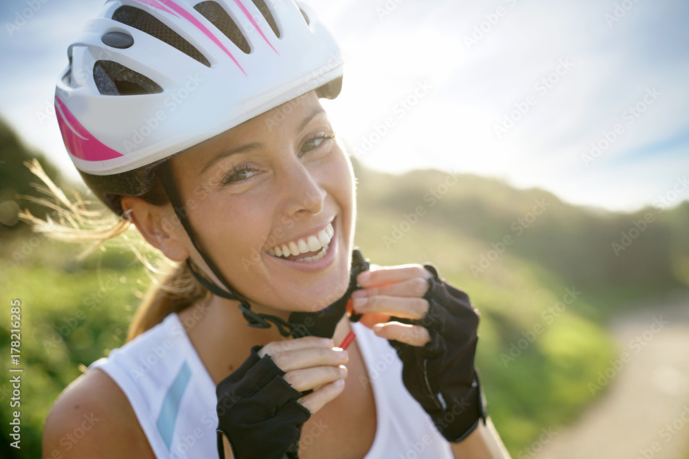 Obraz premium Portrait of smiling woman on bike ride putting helmet on