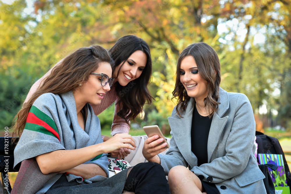 Obraz premium three girlfriends surfing with mobile phone in a park on a bench