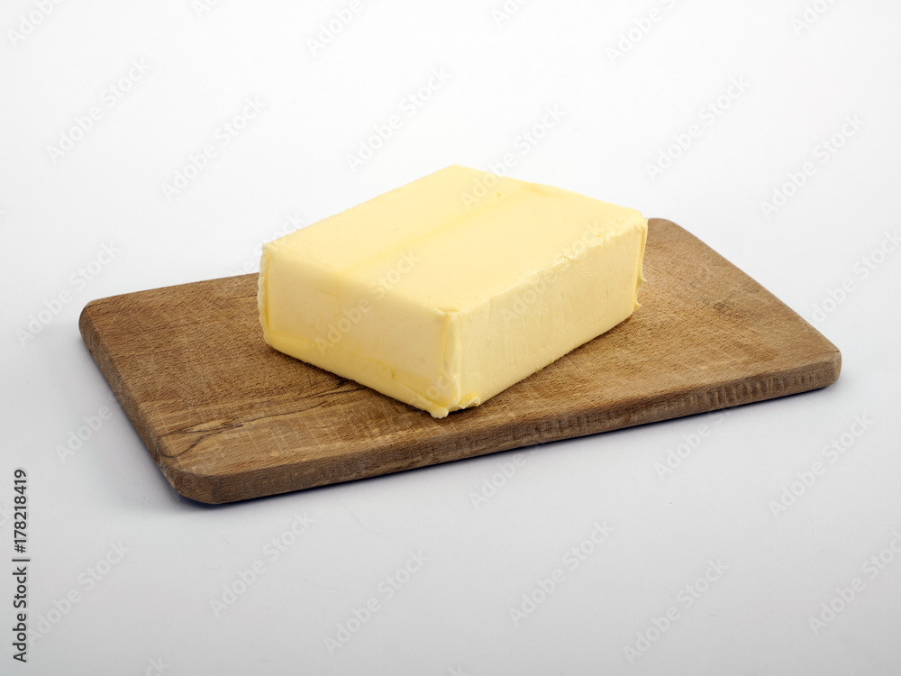 Block of butter on wooden chopping board, white background