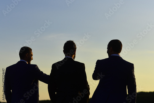 Fotografi Silhouettes of men standing against sunset
