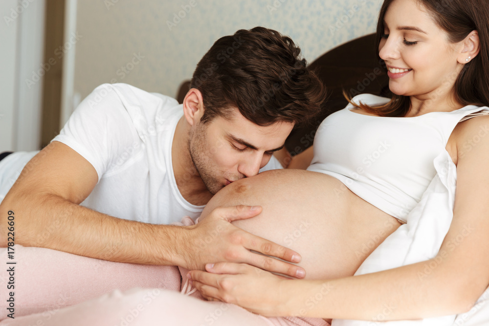 Smiling young pregnant wife lying in bed Smiling young pregnant wife lying in bed