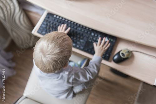 A small child prints on the keyboard in the defocus, the top view photo