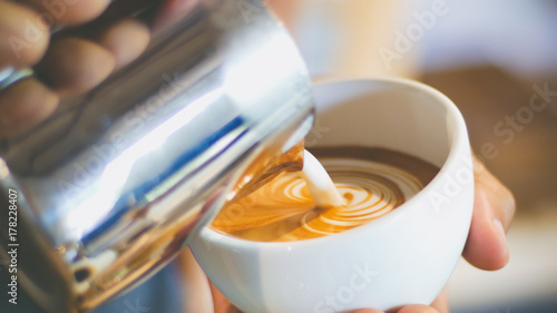 barista pouring streamed milk to make heart shape latte art in cup of hot coffee, retro tone