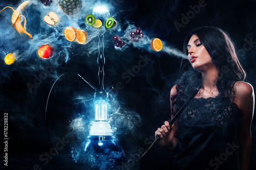 Young, beautiful woman in the night club, bar smoke a hookah or shisha. The pleasure of smoking. Fruits in the smoke. Copy space. Hookah advertisement concept. photo
