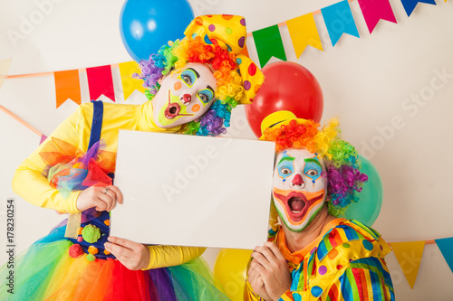 Two clowns boy and girl on holiday with white plate in hands. Birthday of the child.