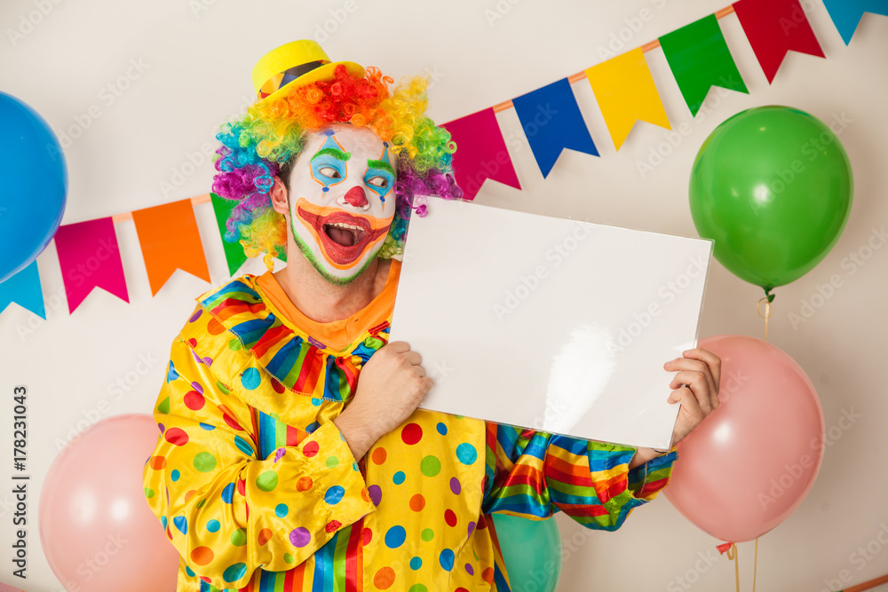 A cheerful, bright clown with a white signboard for the inscriptions in his hands. Birthday of the child. A cheerful, bright clown with a white signboard for the inscriptions in his hands. Birthday of the child.