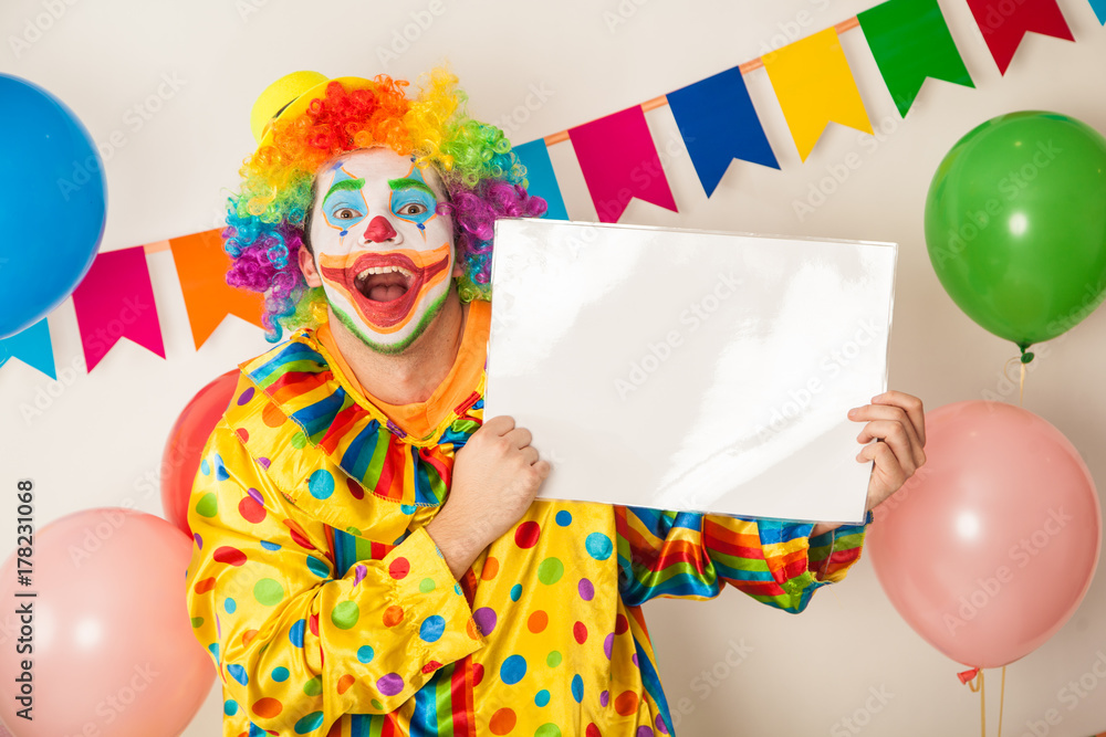 A cheerful, bright clown with a white signboard for the inscriptions in his hands. Birthday of the child. A cheerful, bright clown with a white signboard for the inscriptions in his hands. Birthday of the child.