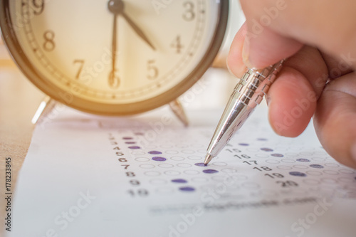 Students taking optical form of standardized exams near Alarm clock with hands holding yellow pen for final examination in school, college university classroom, Education concept