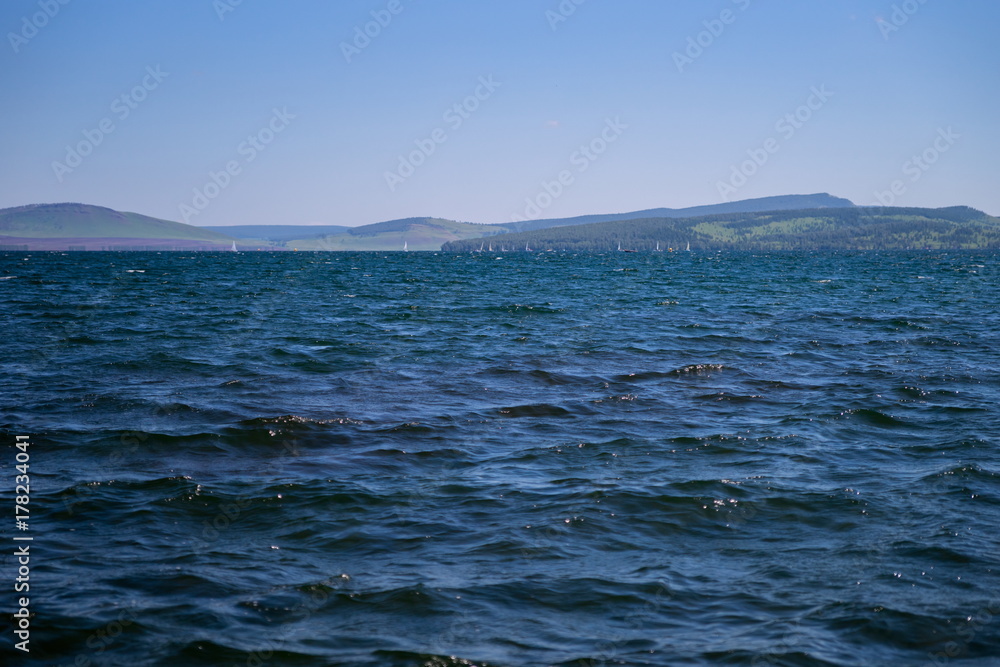 Пейзаж синего озера с парусной регатой вдалеке.