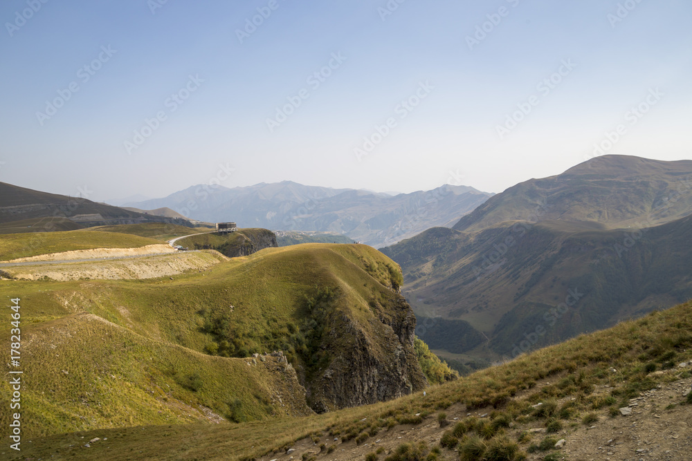 Горный пейзаж, красивый вид на живописные склоны, солнечная погода, белые облака на синем небе, горы и природа Кавказа