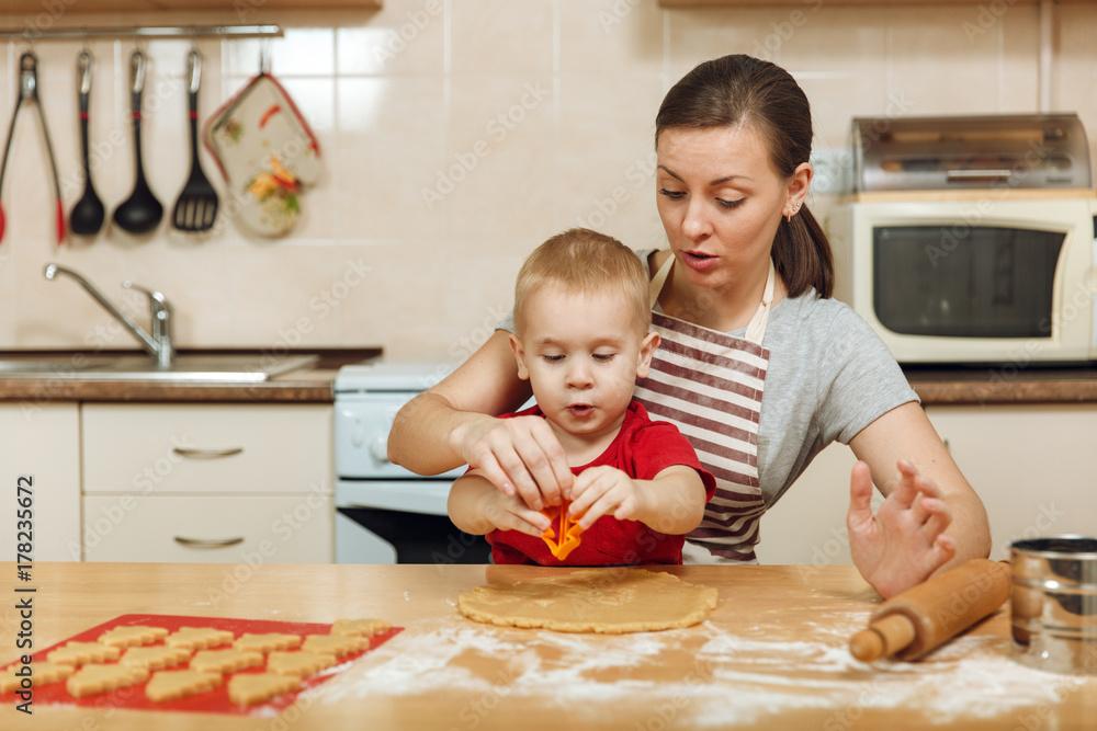 Little kid boy helps mother to cook Christmas ginger biscuit in light kitchen. Happy family mom 30-35 years and child 2-3 roll out dough and cut out cookies at home. Relationship and love concept Little kid boy helps mother to cook Christmas ginger biscuit in light kitchen. Happy family mom 30-35 years and child 2-3 roll out dough and cut out cookies at home. Relationship and love concept