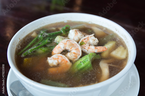 Spicy vegetable and prawn soup in bowl on wooden table