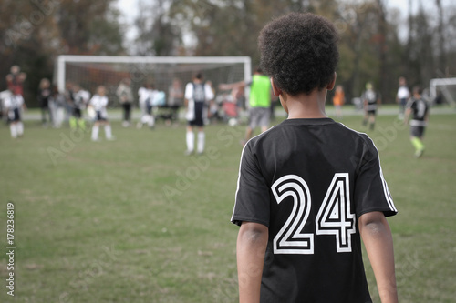 Young african american boy watching friends play football soccer game