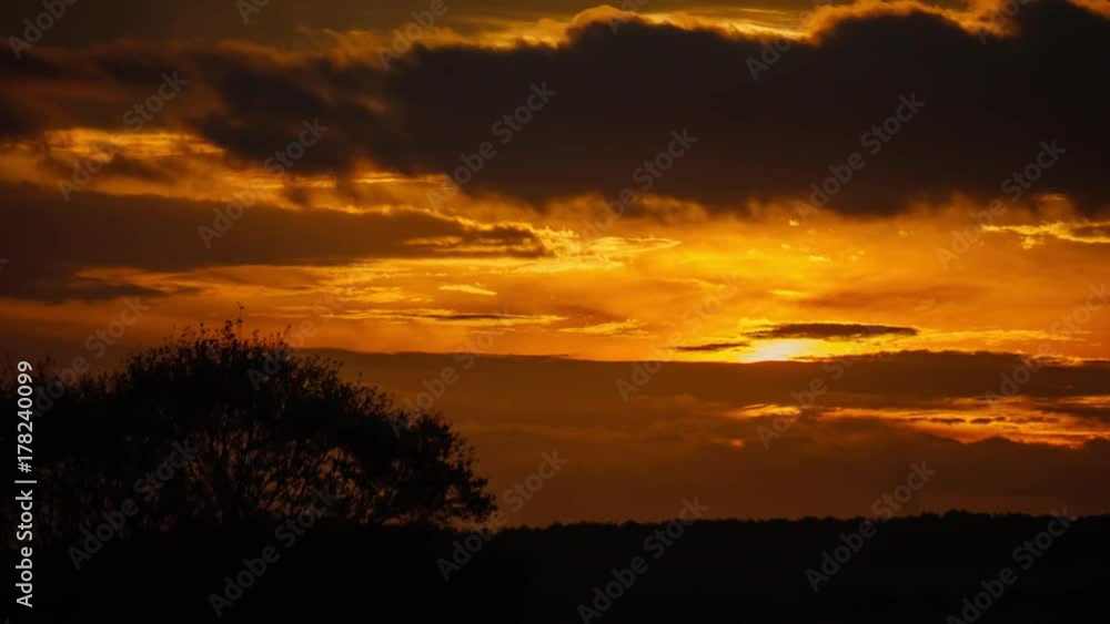 Colourful orange sunset timelapse with dramatic clouds over Oak tree in rural countryside, England. Colourful orange sunset timelapse with dramatic clouds over Oak tree in rural countryside, England.