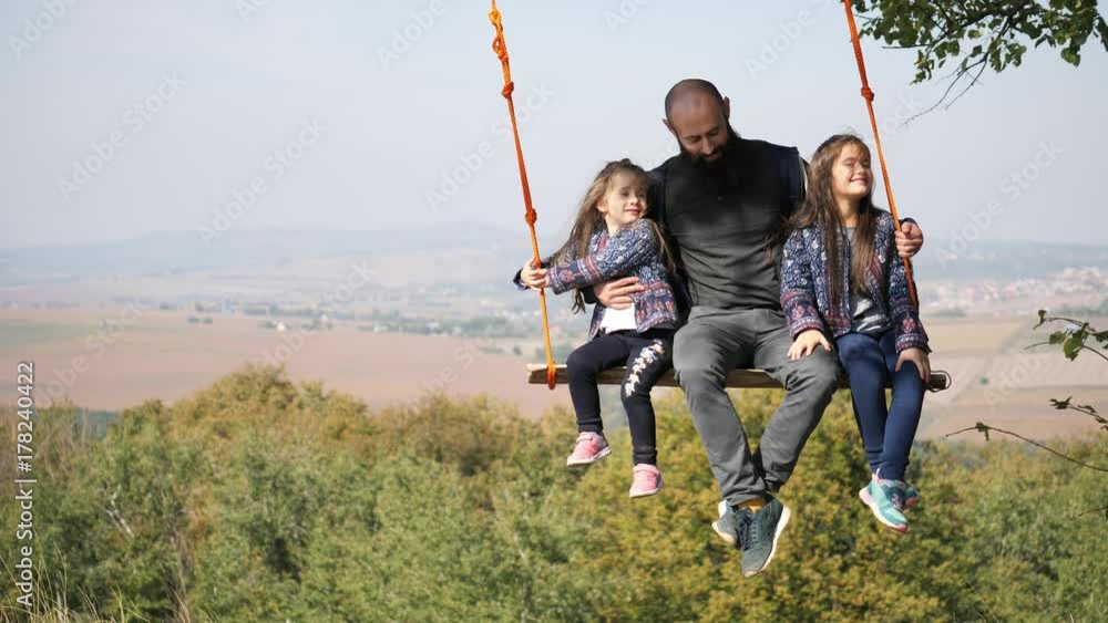 Dad swinging with daughters on a swing under a tree. Dad swinging with daughters on a swing under a tree.