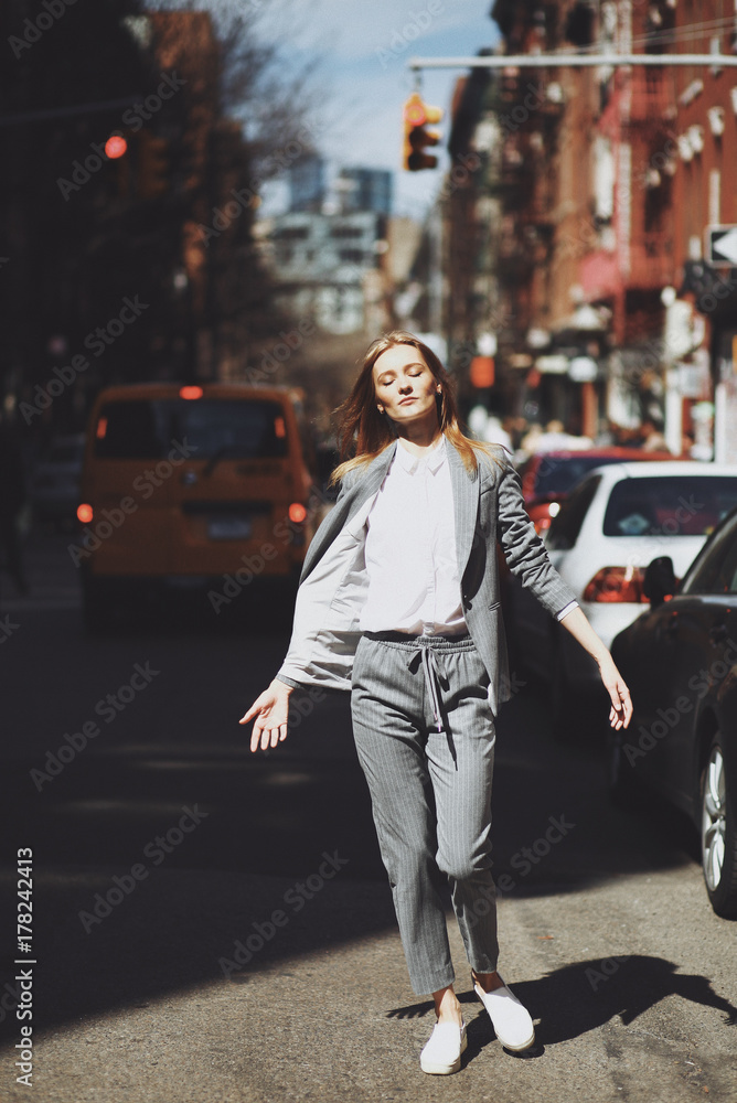 Fototapeta premium Woman in grey suit poses on the street of New York in a windy day