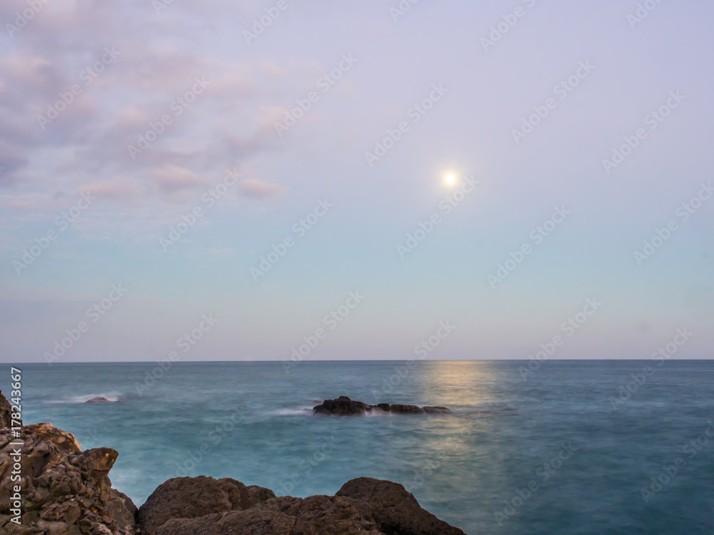 The selective focus of the rock on foreground with the movement of the wave behind. The moon is also shining above of horizontal line of the sea