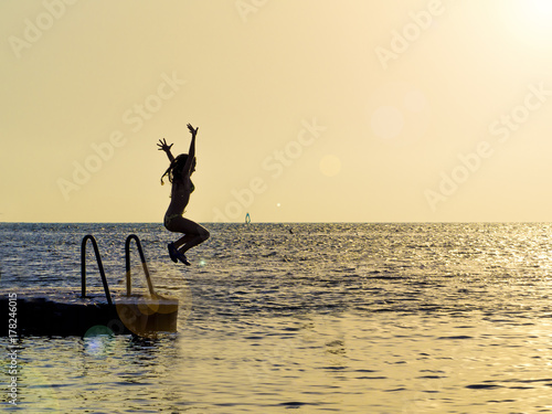 Silhouette of a girl against the sky jumping in the sea on the sunset  concept of happiness