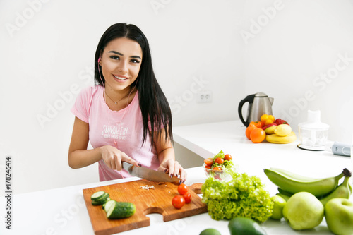 Pretty brunette cuts vegetables on the wooden board and listens to the music in the kitchen