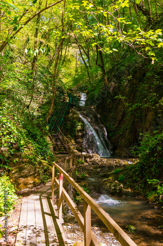 Wooden path and waterfall in the park Berendeyevo Tsarstvo in sunny summer day  Sochi  Russia