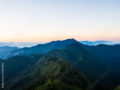 The texture of the green range of mountain ridge of Doi Phu Wae, Nan, Thailand. The hill is still plentiful of green forest. The peak of the hill is beyond the horizontal of sunrise sky