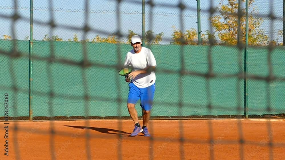 Man playing tennis on clay court, net in front, slow motion Man playing tennis on clay court, net in front, slow motion