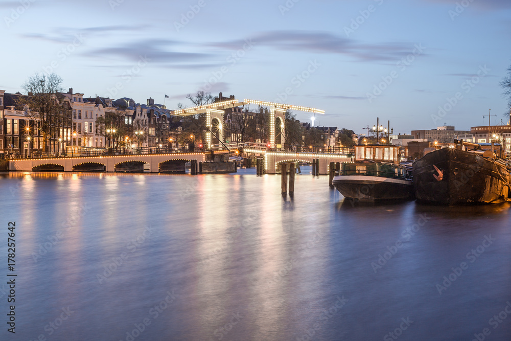 Old historic dutch bridge, Amstel river, and boats in the evening at the twilight blue hour, Netherlands