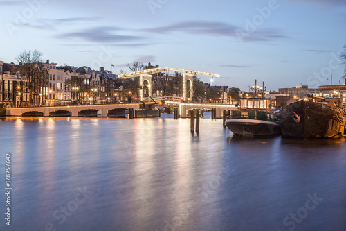 Old historic dutch bridge, Amstel river, and boats in the evening at the twilight blue hour, Netherlands