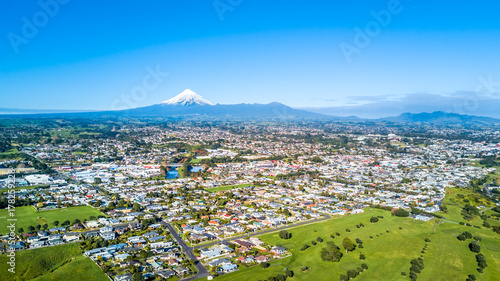 Aerial view on a New Plymouth residential suburb surrounded by green meadow with Mount Taranaki on the background. New Zealand
