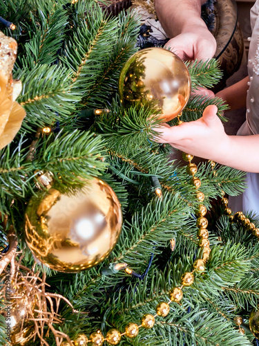 A child and an adult decorate a Christmas tree. A Christmas ball in a child's hand. The symbol of the new 2018 is Yellow Dog. All ornaments should be yellow or gold. Vertical orientation.