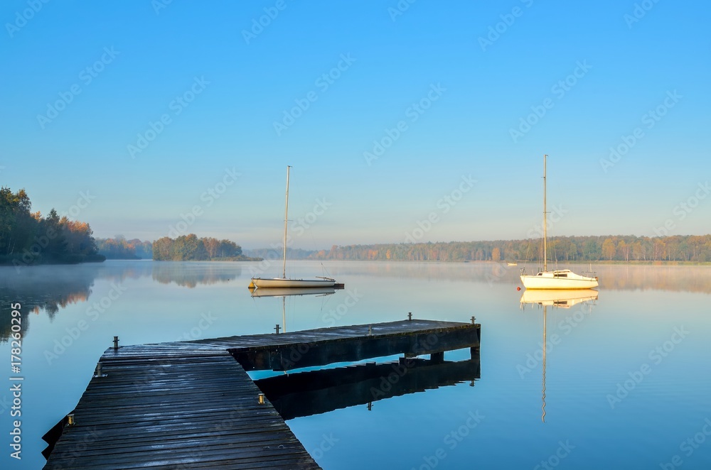 Morning autumn landscape. Wooden pier and boat on a beautiful lake.