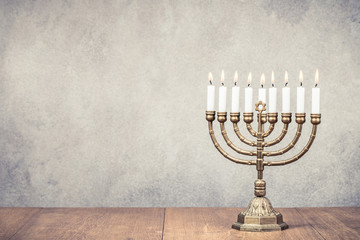 Bronze Hanukkah menorah with burning candles on wooden table front old vintage concrete wall background. Holiday greeting card concept. Retro instagram style filtered photo