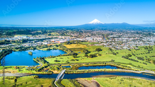 Aerial view on a New Plymouth residential suburb surrounded by green meadow with Mount Taranaki on the background. New Zealand photo