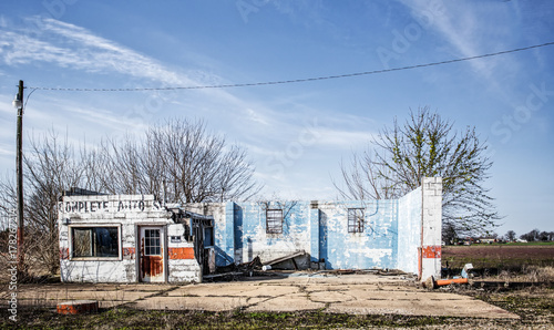 Schilderij op canvas An old crumbled and faded brick auto service center with front wall gone and cem