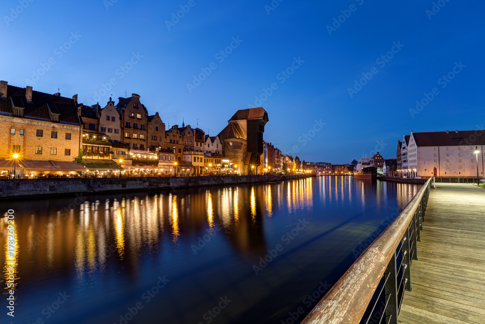 Scenic view of a promenade, lit Crane and other old buildings along the Long Bridge waterfront at the Main Town in Gdansk, Poland, in the evening.