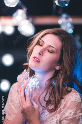 Attractive young caucasian woman poses with string lights with heavy bokeh