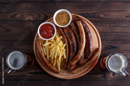 Appetizing grilled sausages and french fries served with spicy tomato ketchup, whole grain mustard and dark beer, flat lay with free space for text design. Oktoberfest food, pub concept
