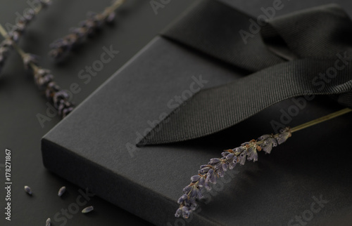 Black gift box on a dark contrasted background, decorated with a textured bow and lavender, creating a romantic atmosphere. Typically used for birthday, anniversary presents, gift cards, post cards, l