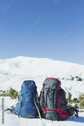 Backpacks stand in the snow against the backdrop of the mountains.