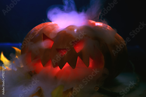 Halloween pumpkin lantern with dry leaves with burning eyes